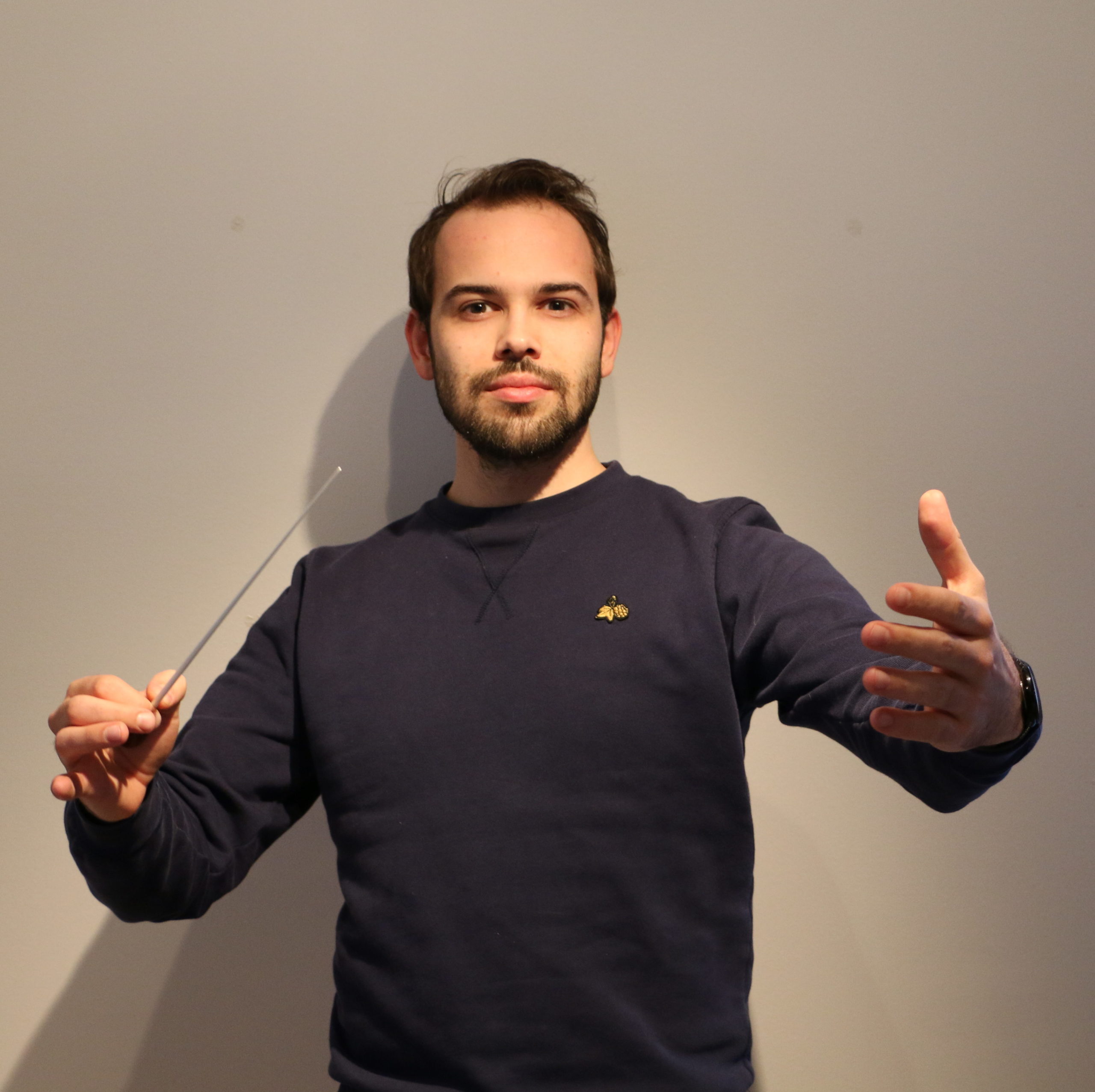 Benedikt Migge dirigiert. In der rechten Hand hält er einen Taktstock.